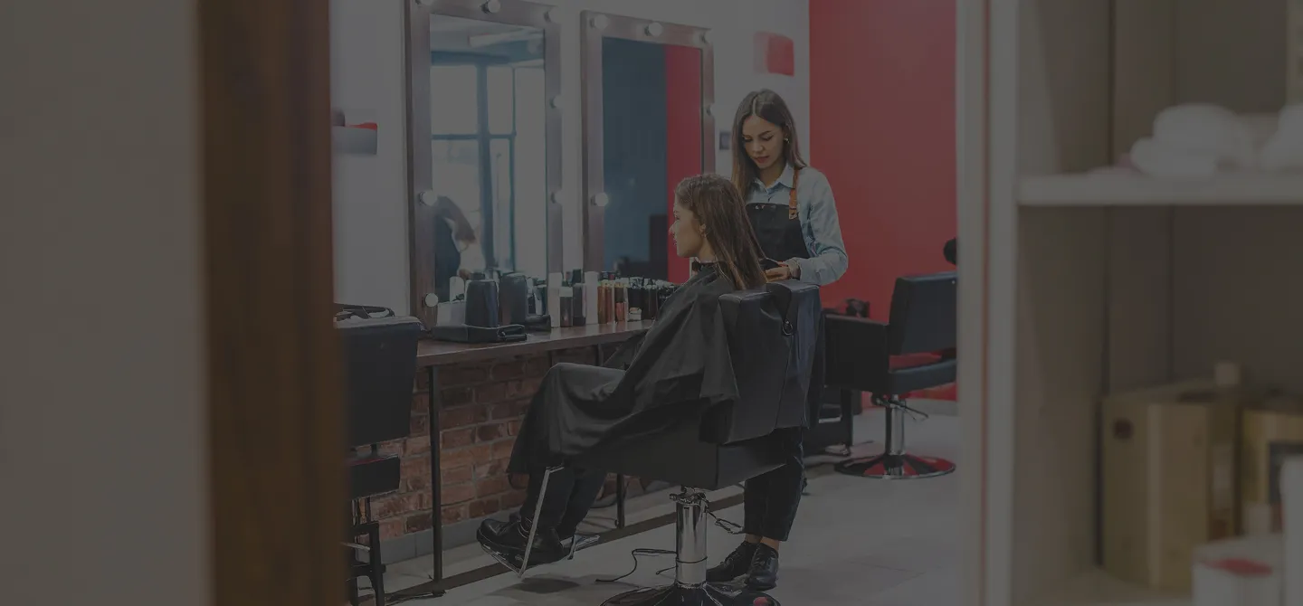 Pequeño salón de belleza donde un peluquero corta y peina el cabello de una clienta.